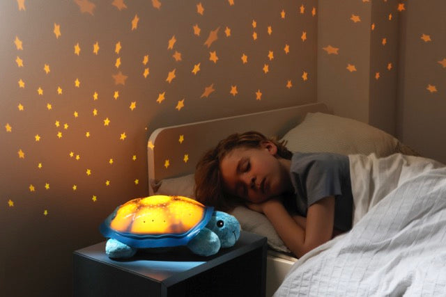 Child sleeping with Cloud b Twilight Turtle projecting warm amber stars onto the wall
