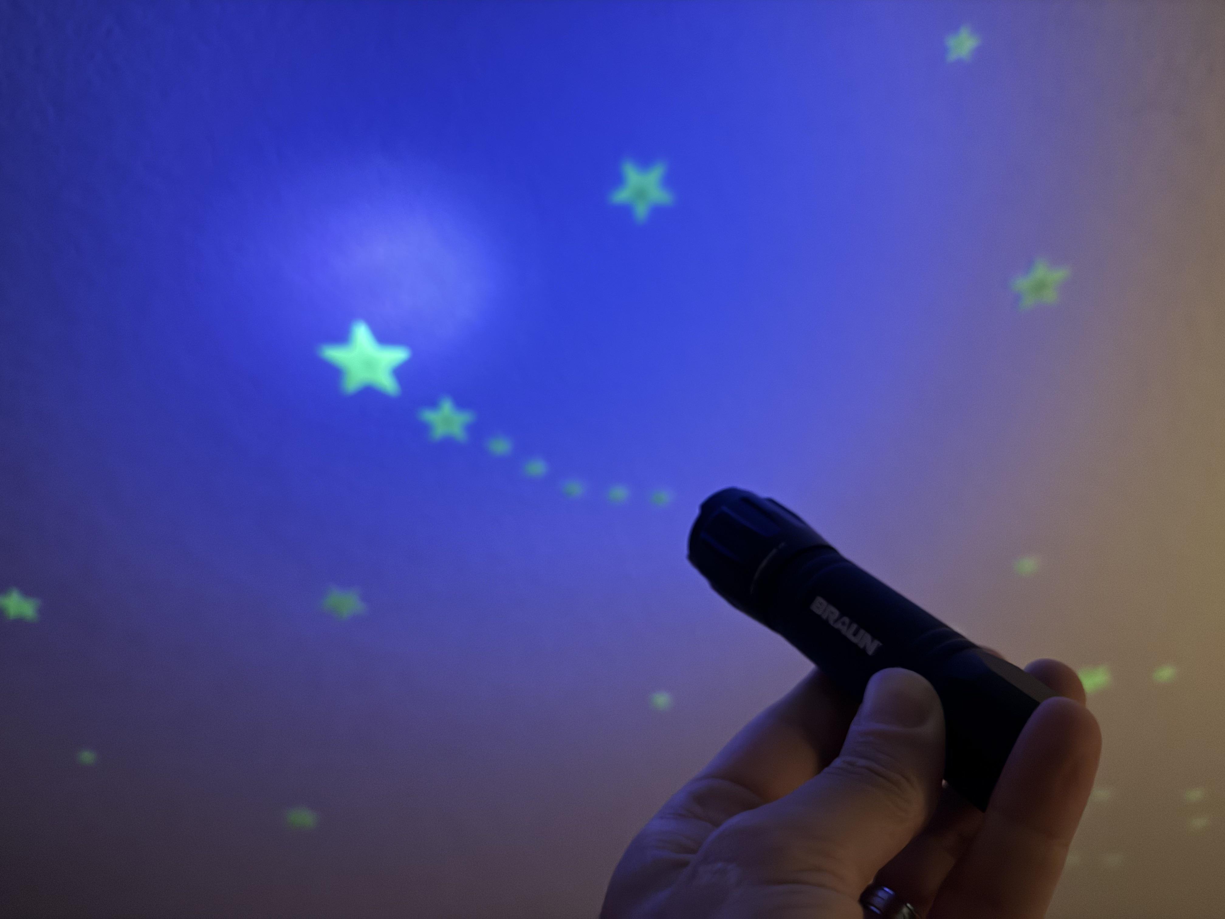 Glow in the dark stars on a bedroom ceiling being charged with a UV flashlight